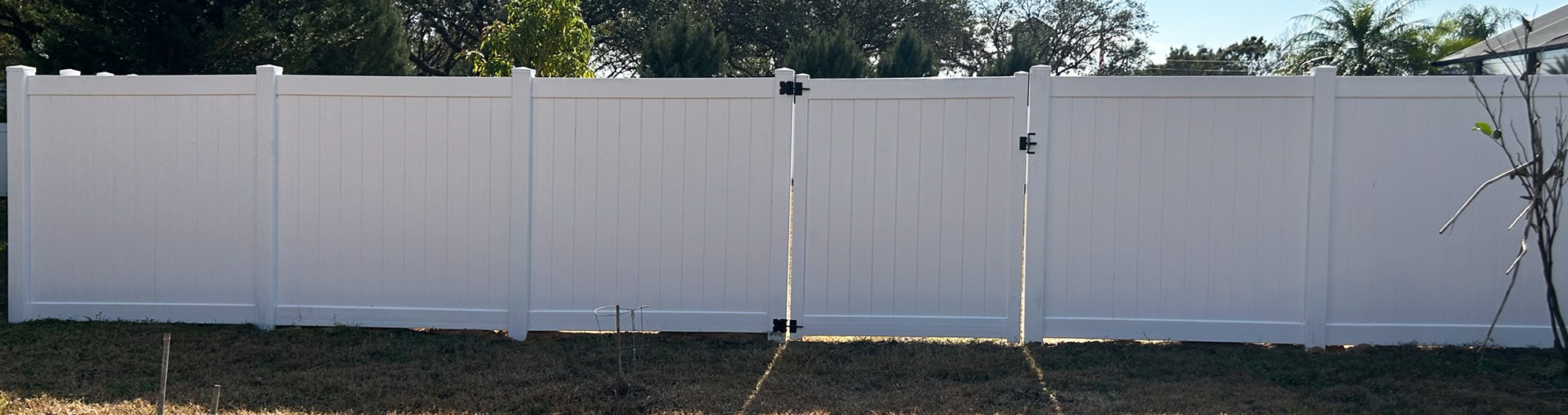 bftb21_03 White vinyl privacy fence with a walk gate and trees behind it.